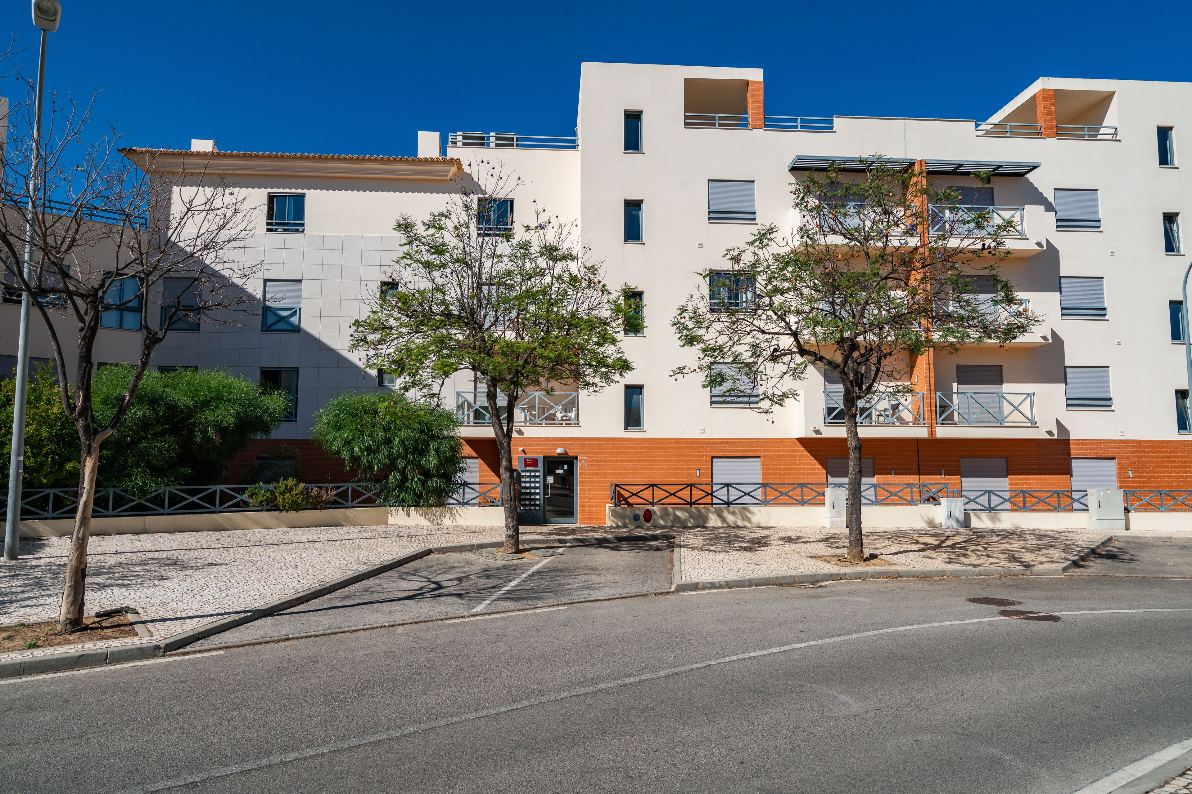 A modern building with multiple floors, balconies, and a parking area.