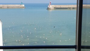 Une vue sur la mer, prise depuis une fenêtre ornée d’une balustrade, avec un phare et une côte lointaine.