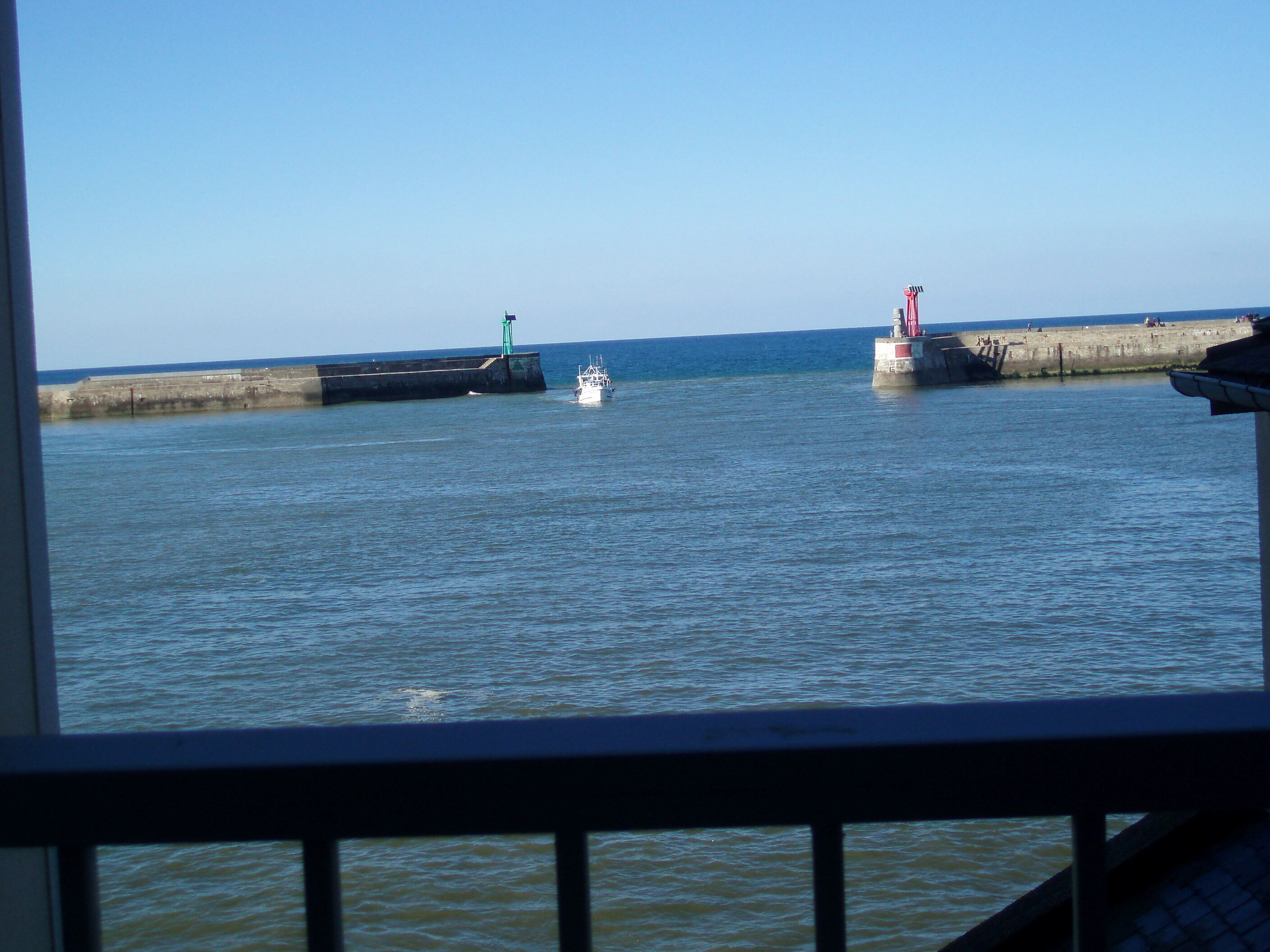 Ein ruhiges Ufer mit einem kleinen Boot, einem grün-roten Leuchtturm und einem Betonsteg.