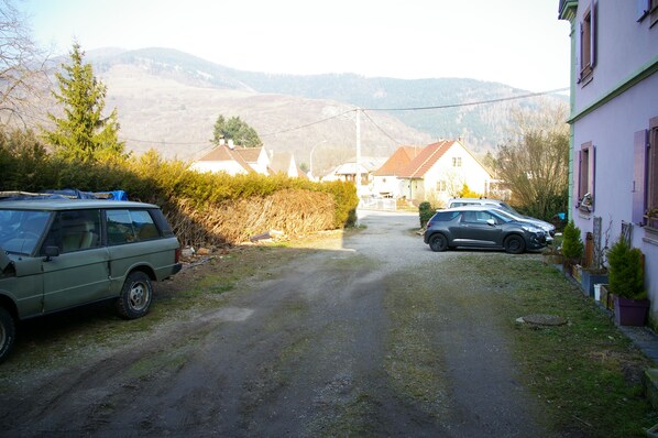 Eine ländliche Straße mit geparkten Autos, Häusern und Bergen im Hintergrund.