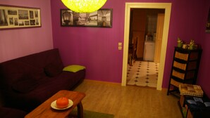 A living room with a purple wall, a wooden table with a plate of fruit, a sofa, and a doorway leading to a kitchen. - Apartment 6-10 p, quiet, close to resorts and nature, Wifi, cleaning and sheets included (Fellering)