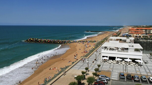 A beach with umbrellas, a rocky breakwater, and a parking lot with cars. - Comfortable T2 Beach/Pool/Golf/Thalasso (Anglet)