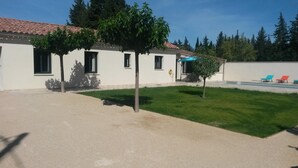 Un bâtiment avec un toit recouvert de tuiles, une pelouse verdoyante et une piscine équipée de chaises longues.