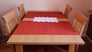 A wooden dining table with a red tablecloth and four wooden chairs.