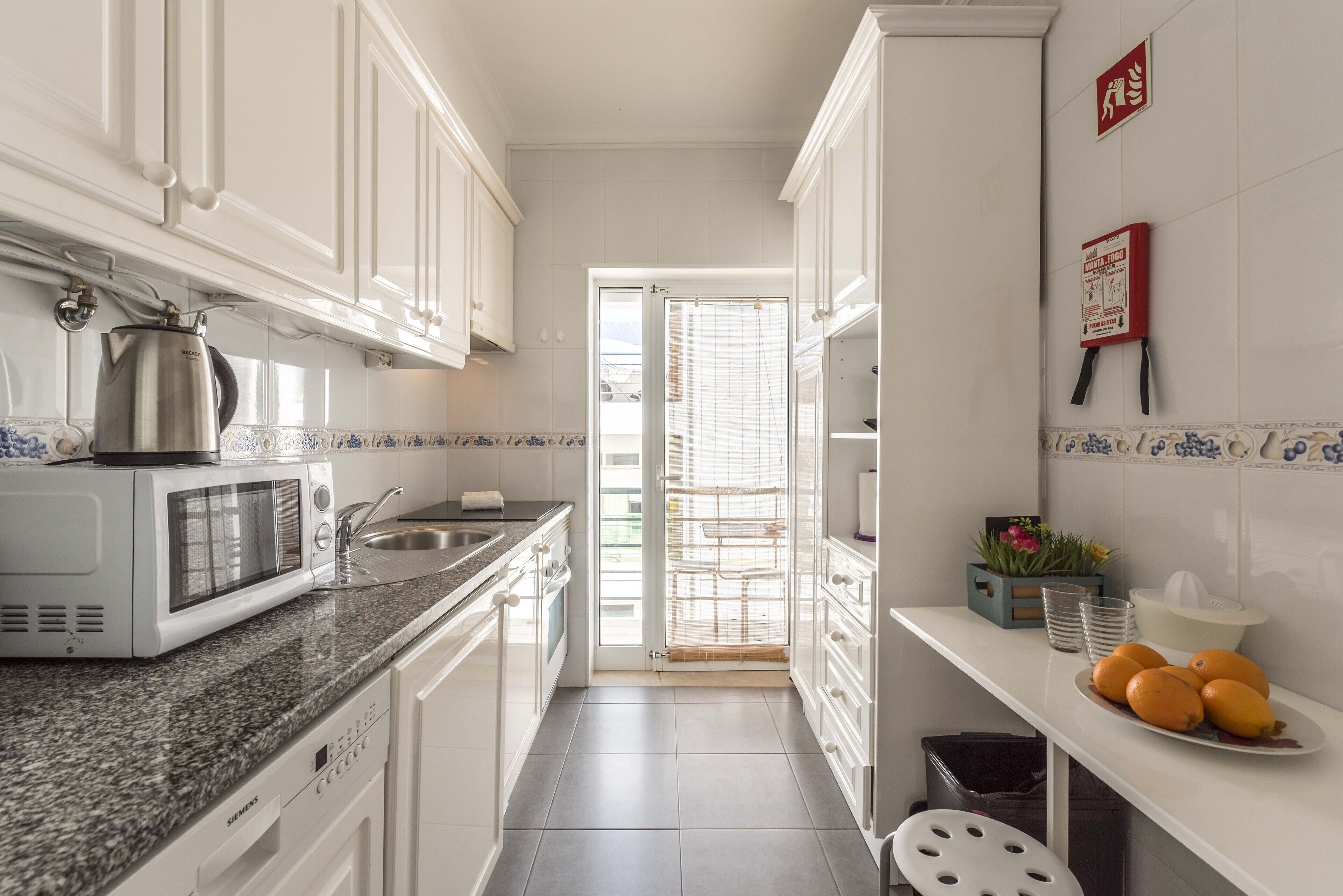 A kitchen with white cabinets, a microwave, a sink, and a door leading to a balcony.