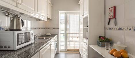 A kitchen with white cabinets, a microwave, a sink, and a door leading to a balcony.
