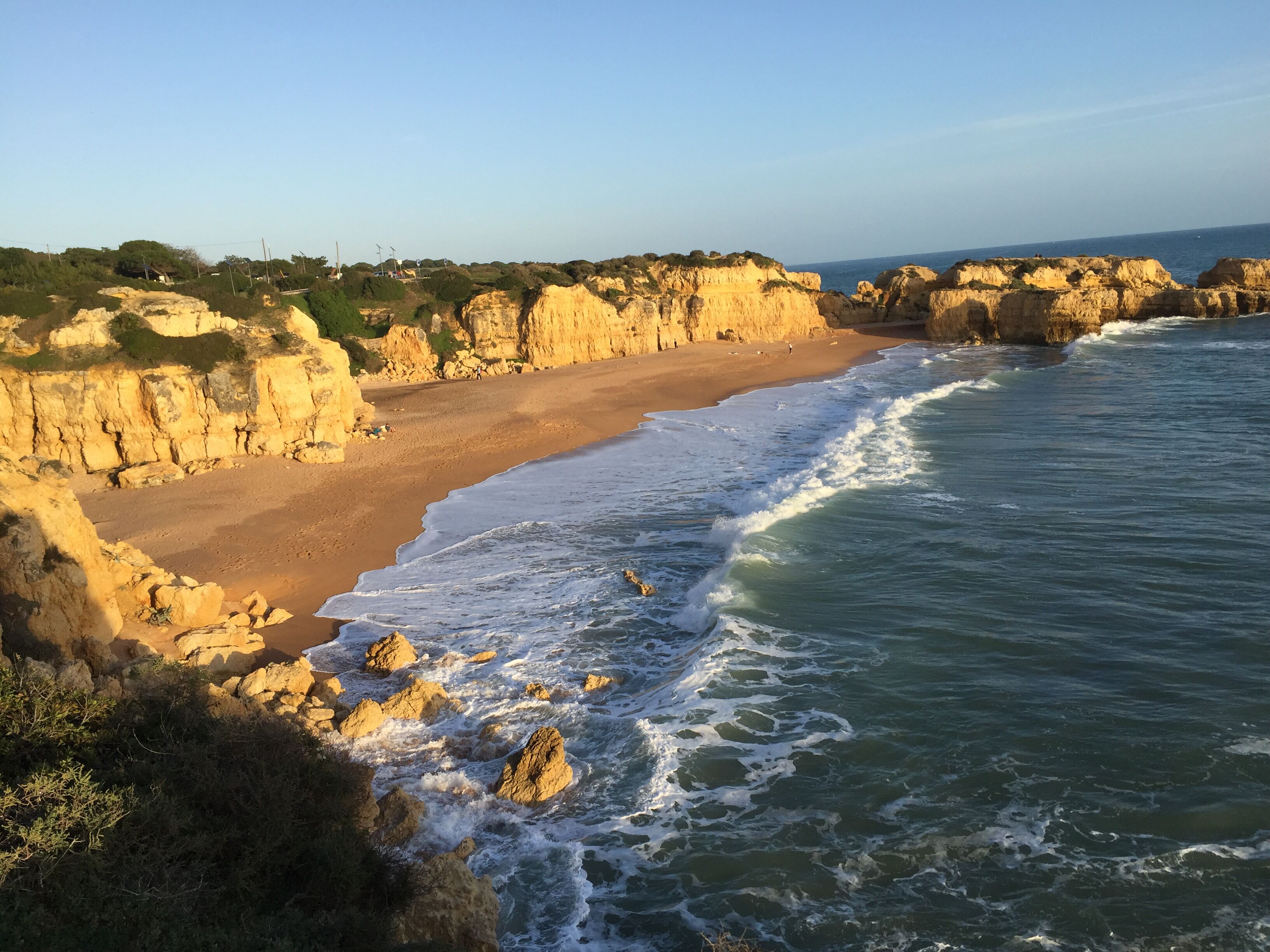 Un paisaje costero con una playa arenosa, acantilados rocosos y olas.