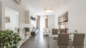 Un salon moderne avec une table basse en verre, des canapés de couleur beige et un coin repas avec des chaises.