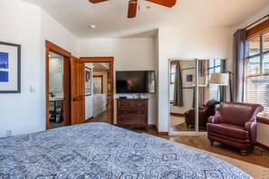 Un dormitorio con una cama grande, televisión, espejo, una silla y armario.