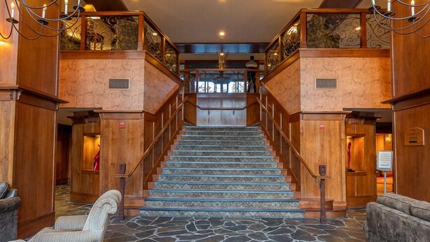 Un grand escalier avec un sol en pierre menant à un deuxième niveau, flanqué de rampes en bois et de lustres.