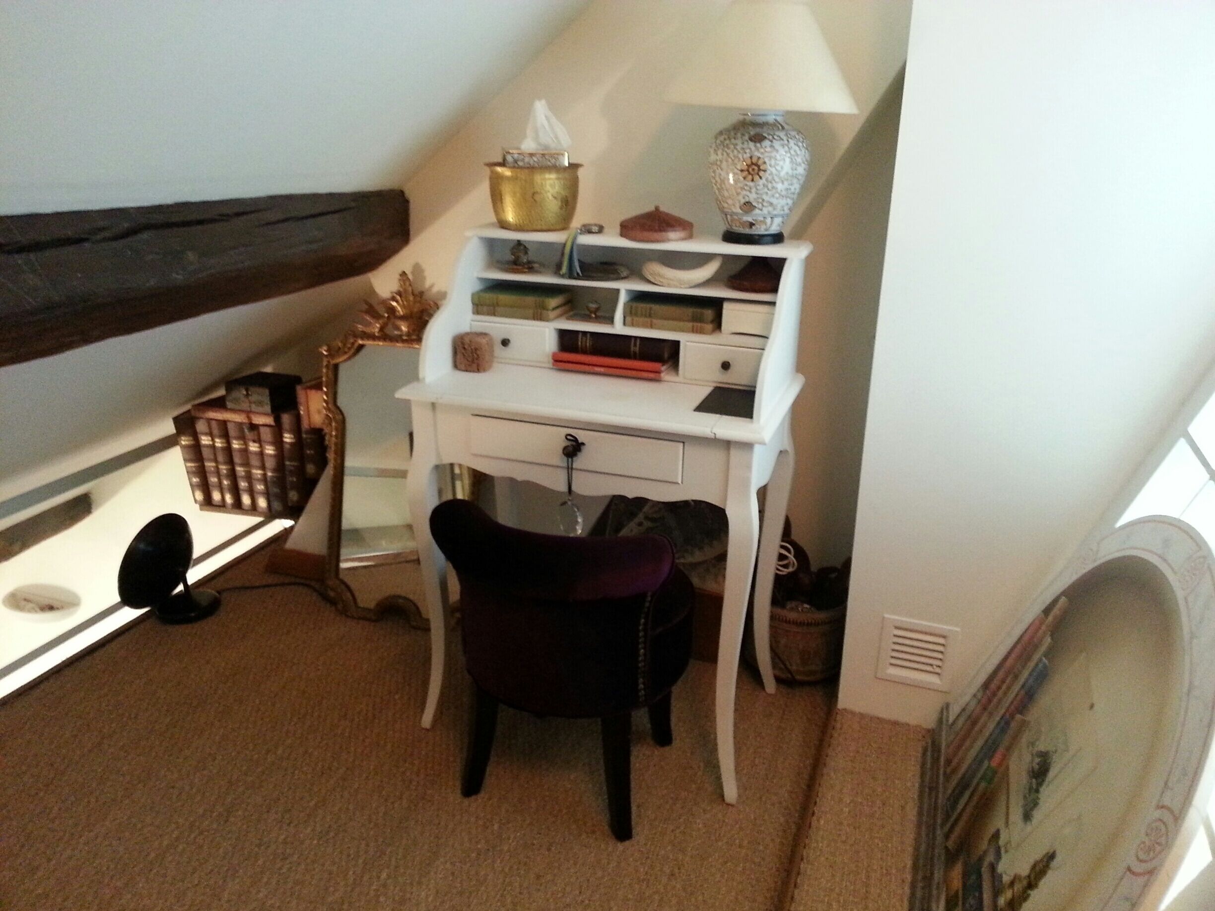 A small study room with a white desk, a chair, a lamp, and a bookshelf.