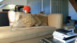 A living room with a beige sofa, a small table with books, and a decorative vase.