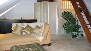 A cozy living room with a sofa, a coffee table, a kitchen area, and a staircase.