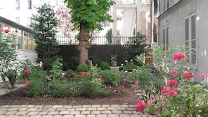 A garden with various plants and flowers, a tree, and a brick pathway.