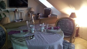 A dining table set for four with a white tablecloth, surrounded by four chairs. A television is mounted on the wall above the table.