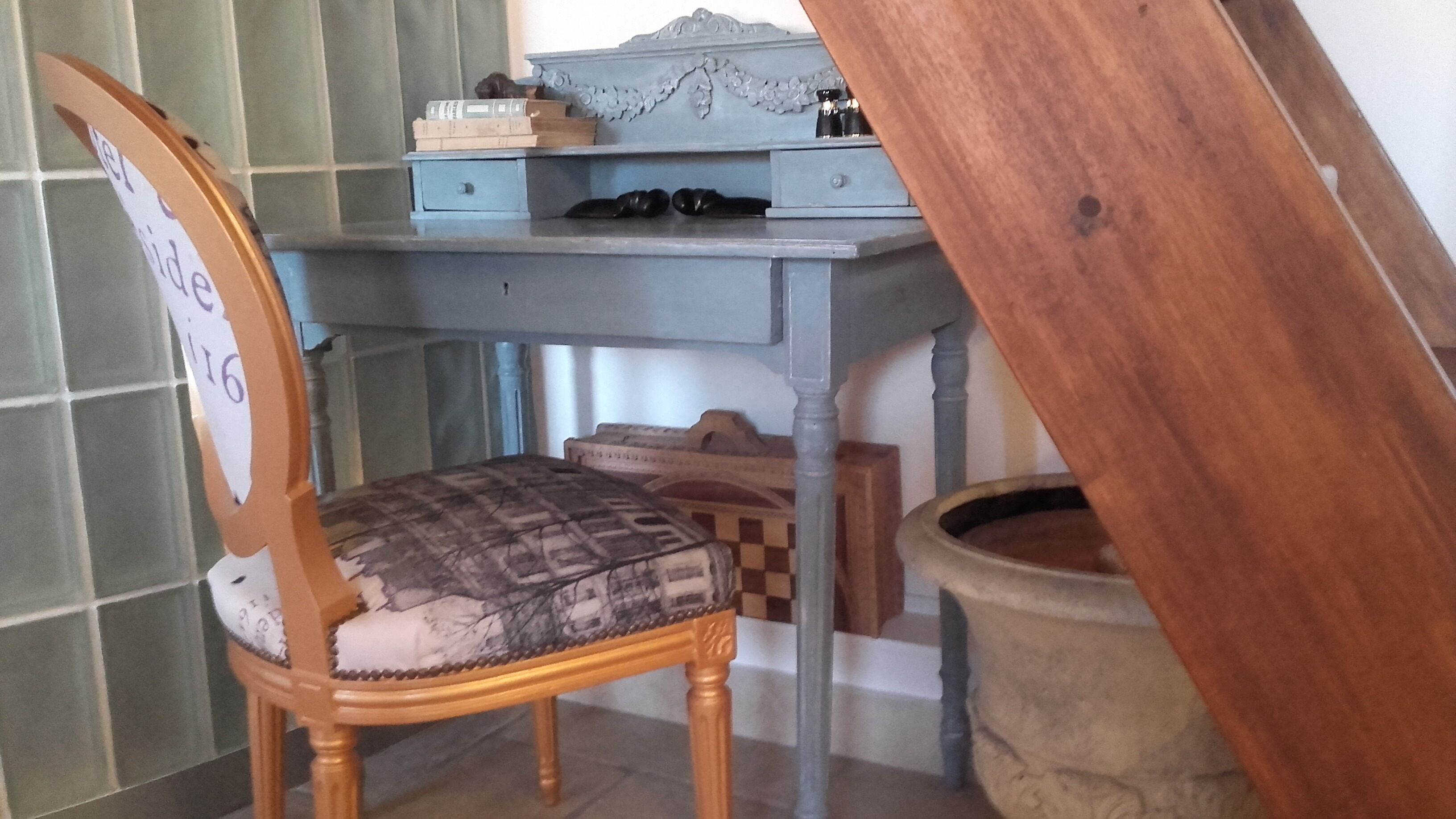 Een houten stoel met een kussen, een bureau met een blauwe blad en een houten kruk.
