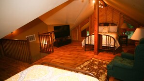 Ein Schlafzimmer im Dachgeschoss mit Holzboden, einem Bett, einem Fernseher und einem grünen Sessel.