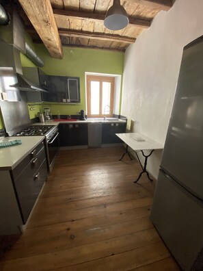A kitchen with wooden flooring, a stainless steel refrigerator, a stove, and a sink.