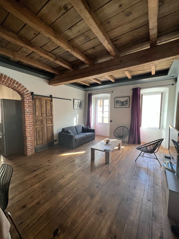 A spacious living area with wooden flooring, a brick fireplace, a sofa, a coffee table, and a television. - Right in the center of Ile-Rousse, the beach at your feet (L'île-Rousse)