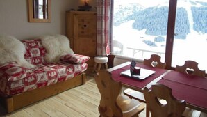 Une pièce chaleureuse avec un canapé en bois, une table à manger avec des chaises, un buffet en bois et une grande fenêtre donnant sur un paysage enneigé.