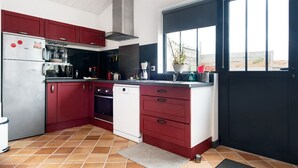 Une cuisine avec des meubles de couleur rouge, un réfrigérateur en acier inoxydable, un lave-vaisselle et une fenêtre donnant sur la plage.