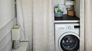 Une buanderie équipée d’un lave-linge, d’un étendoir et d’une étagère où sont rangés les produits de toilette.