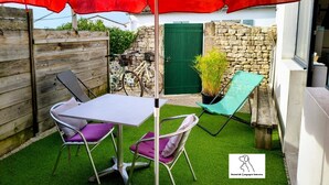 Une terrasse avec une table et des chaises, un parasol rouge et un mur en pierre.
