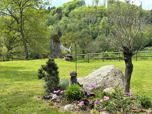 Un jardin avec un grand rocher, un petit arbre et des fleurs roses.