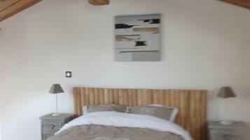 Een slaapkamer met een houten plafond, een bed met een wit-beige dekbedovertrek, twee nachtkastjes met lampen, en een schilderij aan de muur.