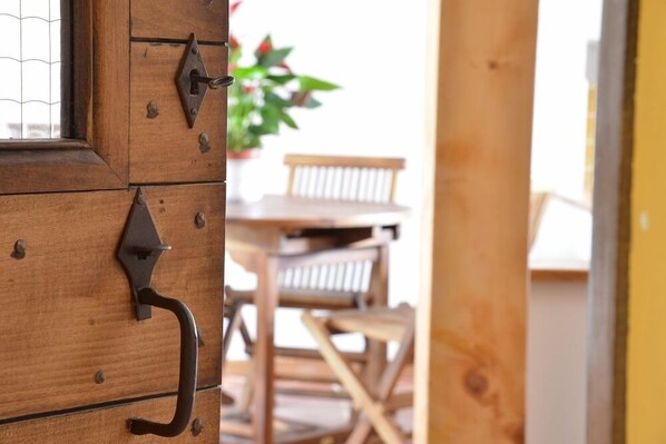 Puerta de madera con manija y pestillo de metal, que da acceso a un área exterior con mesa y sillas de madera.