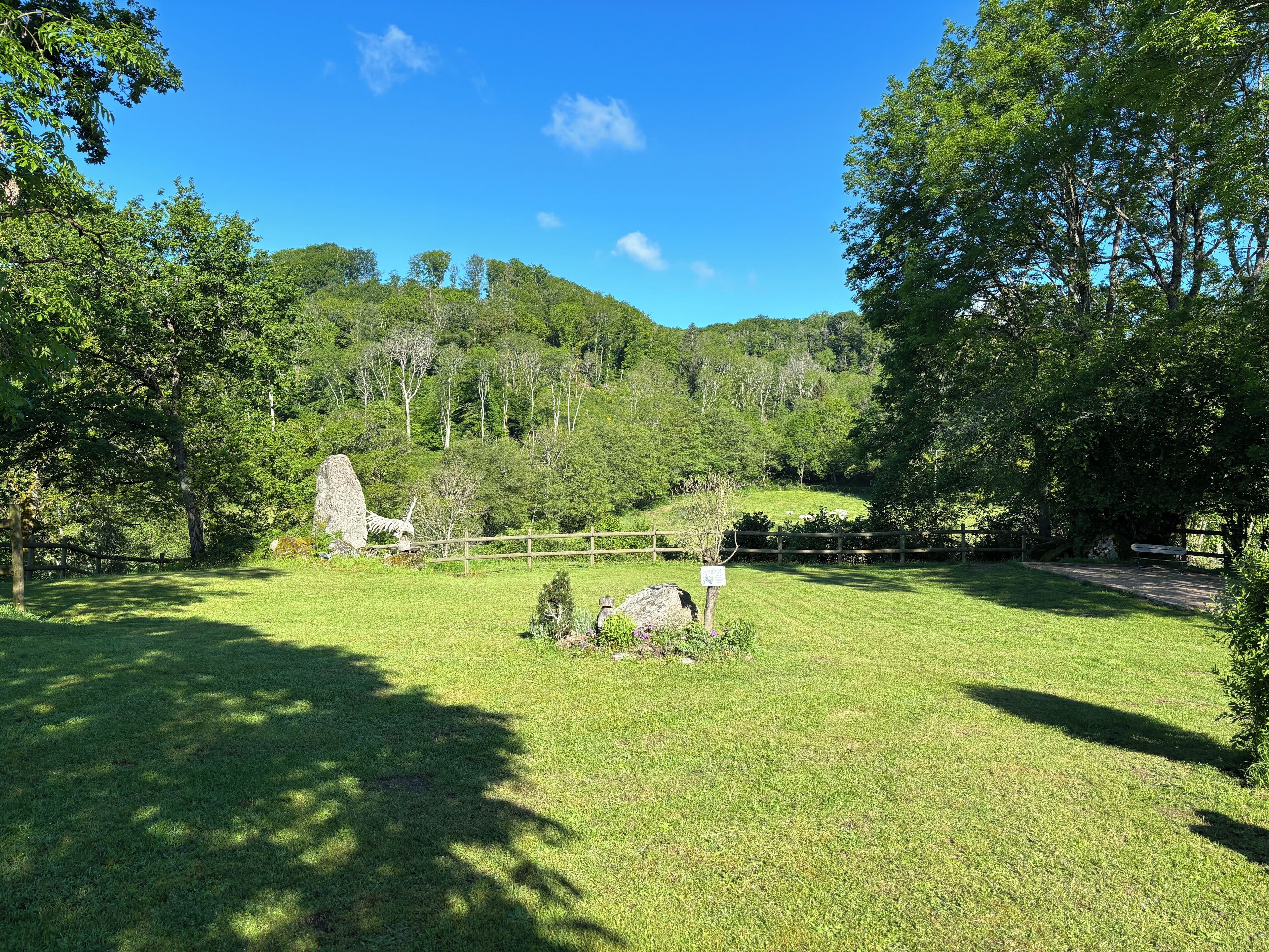 Un champ herbeux avec une clôture en bois, des arbres et une colline en arrière-plan.