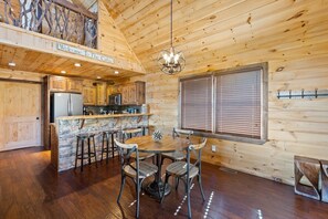 A cabin interior with a stone accent wall, wooden ceiling, a bar area, and a dining table with chairs.