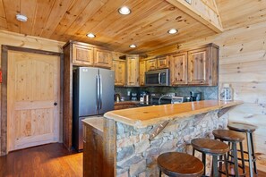 A wooden cabin interior with a stone island bar, wooden cabinets, a refrigerator, and a microwave.