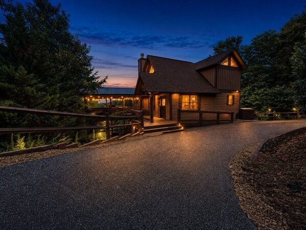 A two-story wooden house with a porch, surrounded by trees.