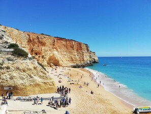 A beach with a rocky cliff, clear blue water, and a sandy shore. - Fantastic apartment for lovers, friends or family vacations (Albufeira)