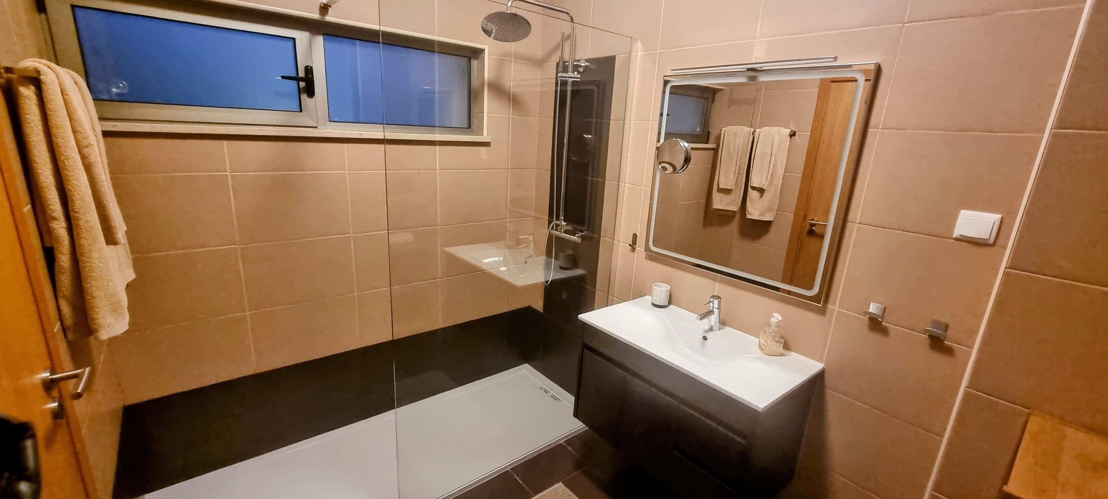 A bathroom with a shower, a sink, a mirror, and a window.