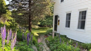 Un chemin de jardin menant à une maison blanche dont la base est bordée de pierres.