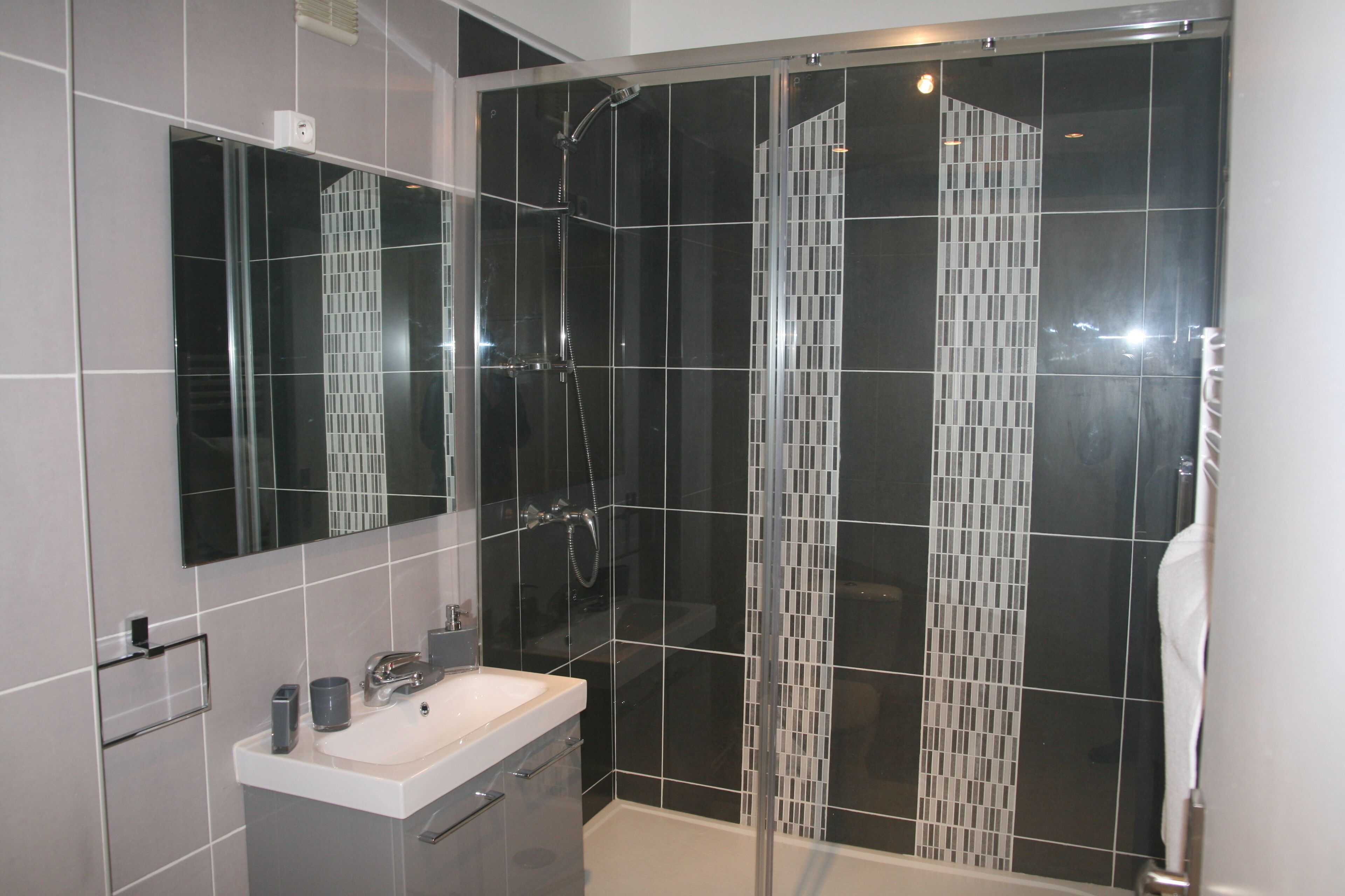 Een moderne badkamer met een douchecabine van glas, een witte wastafel en een grote spiegel.