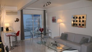Ein modernes Wohnzimmer mit einem Glastisch, einem grauen Sofa und einem Essbereich mit klaren Stühlen und einem Glastisch.