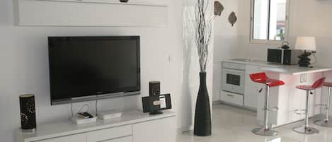 A modern kitchen with a flat-screen TV, a vase with branches, and two red bar stools.