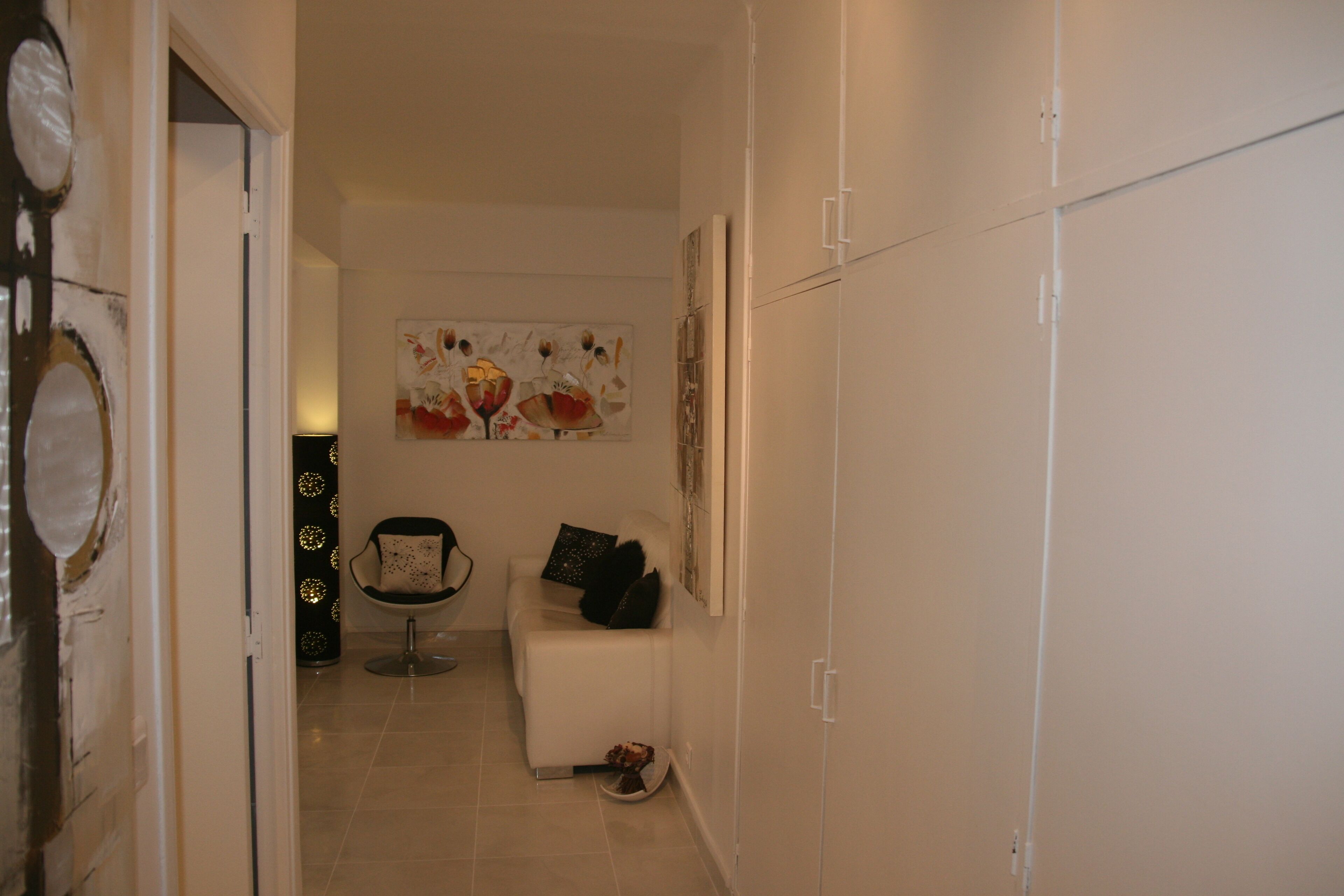 A hallway with a white wardrobe, a chair with a black cushion, and a wall-mounted artwork.