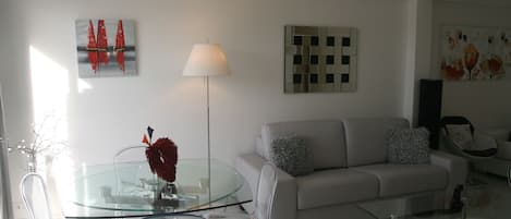 Ein modernes Wohnzimmer mit einem Glastisch, klaren Stühlen, einem grauen Sofa und einer Stehlampe.