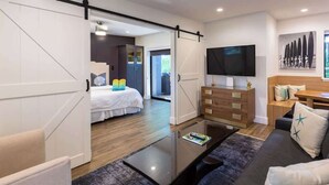 Une chambre d’hôtel moderne dotée d’un grand lit, d’un téléviseur à écran plat, d’une commode en bois et d’une porte coulissante donnant sur un balcon.