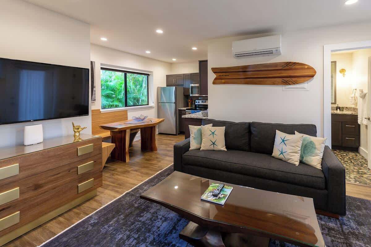 A modern living room with a flat-screen TV, wooden furniture, a sofa with decorative pillows, and a dining area with a table and chairs.