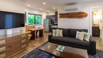 A modern living room with a flat-screen TV, wooden furniture, a sofa with decorative pillows, and a dining area with a table and chairs.