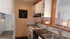 Una cocina compacta con armarios blancos, estufa, fregadero y una cabeza de venado decorativa en la pared.