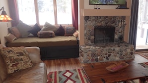 Una sala de estar con chimenea de piedra, un sofá, una mesa de centro y un televisor sobre la chimenea.