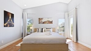 A bedroom with a large bed, a painting of the Eiffel Tower, and a view of greenery outside. - Buddha Estate, Pool , Spa, Sauna, Game Room (Las Vegas)