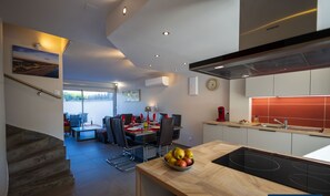 Een moderne keuken met een inductiekookplaat, een eethoek met een tafel voor vier personen, en een trap naar een hoger niveau.