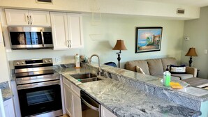 A modern kitchen with stainless steel appliances, a granite countertop, and a dining area with a sofa and lamps.
